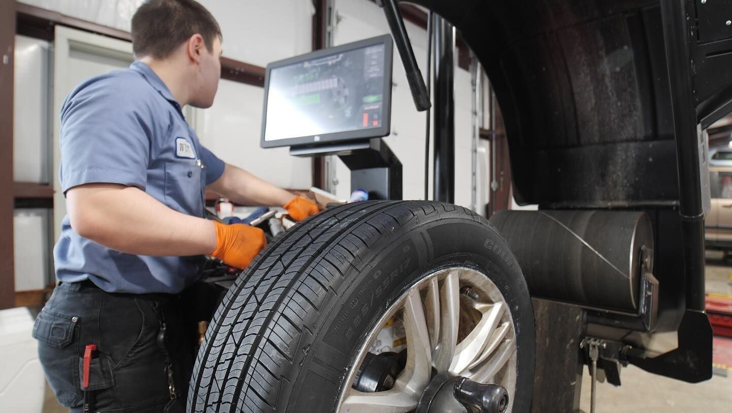 A man is balancing a tire on a machine in a garage.