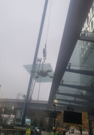 A crane is lifting a glass canopy over a building