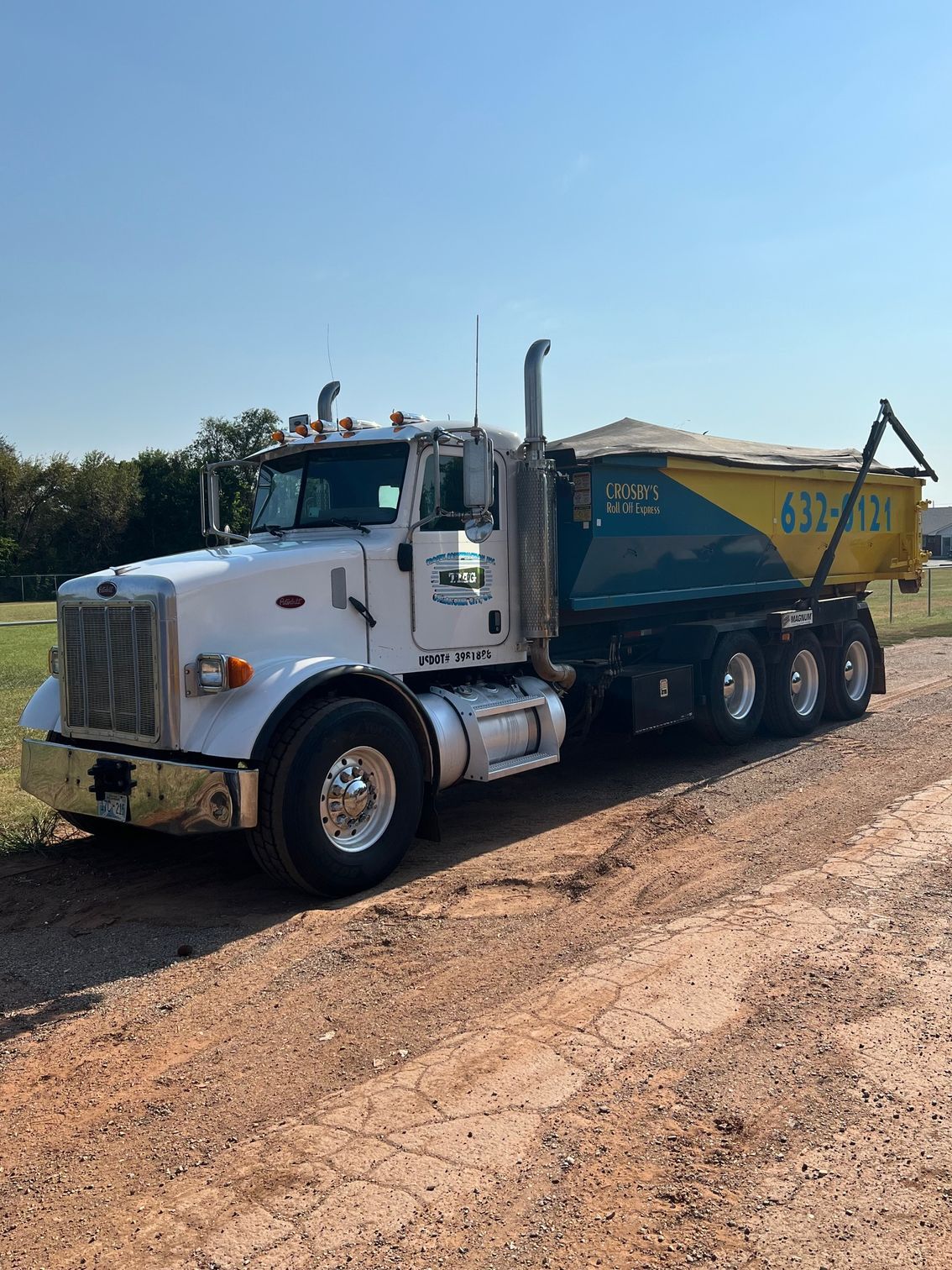 White dump truck on a dirt road, blue and yellow dump bed.