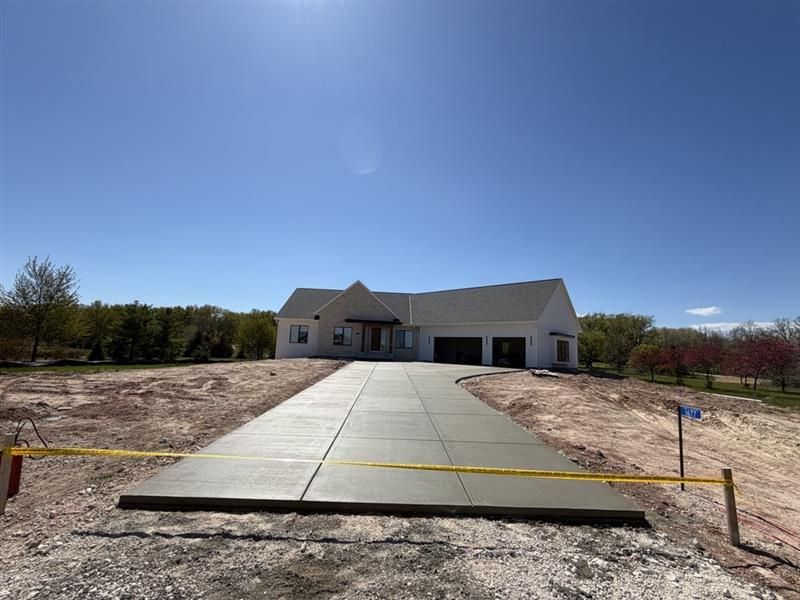 Single-story white house under construction with a long concrete driveway leading to the front entrance