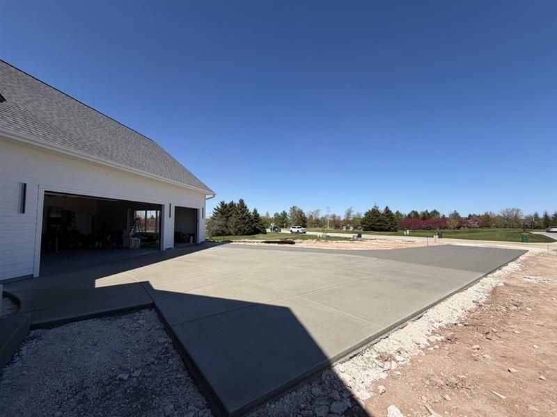 Fresh concrete driveway beside a white garage under a clear blue sky