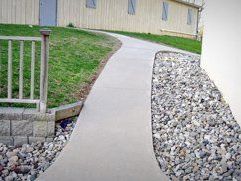A concrete walkway next to a fence and a pile of gravel.