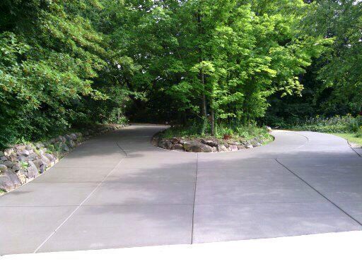 A concrete driveway is surrounded by trees and rocks.