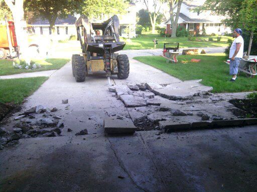 A man is standing in front of a concrete driveway that has been damaged by a bulldozer