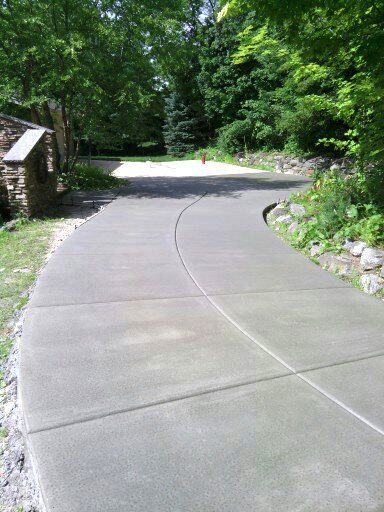 A curved concrete driveway leading to a house surrounded by trees.