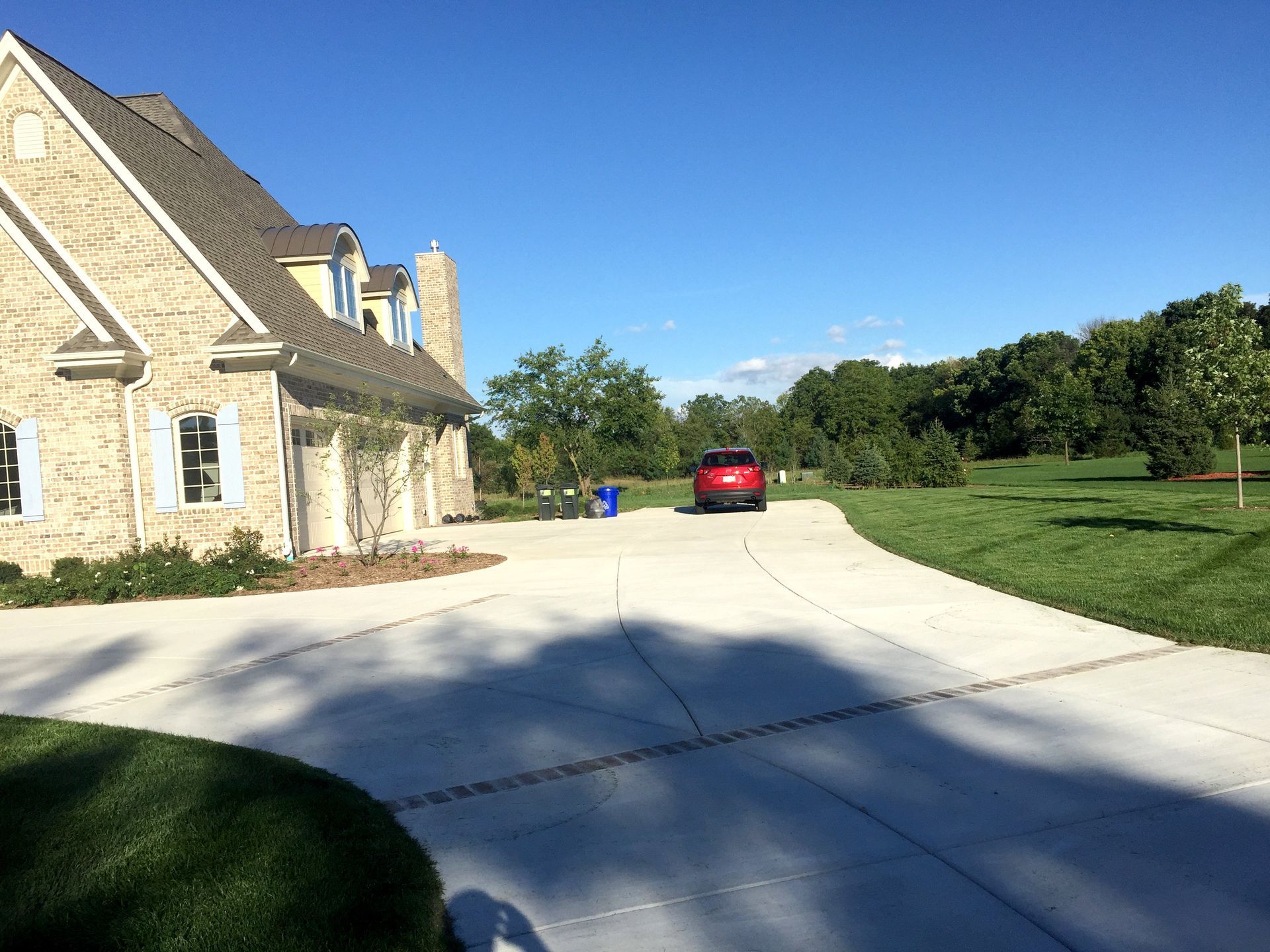 A red car is parked in a driveway in front of a large house.