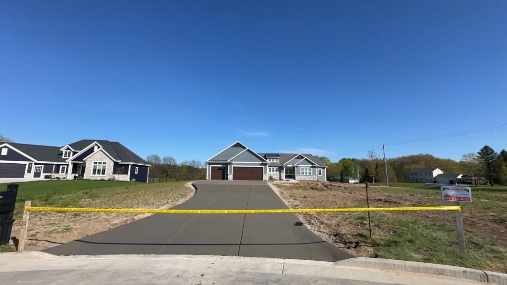 A concrete driveway with a yellow tape blocking it and a house in the background.