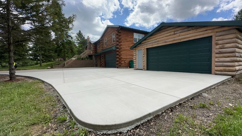 A log cabin with a concrete driveway in front of it.