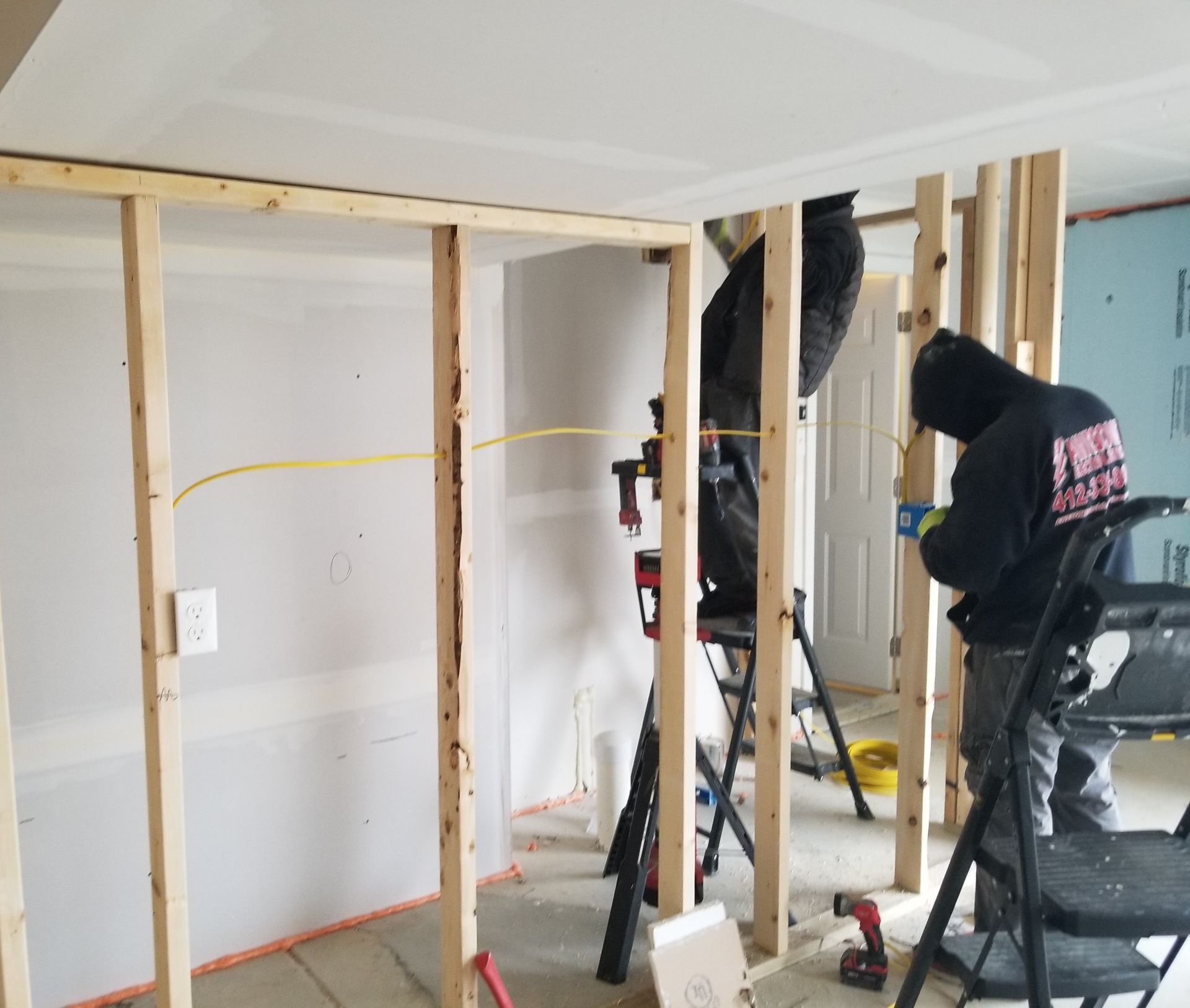 People framing a wall in an unfinished room with exposed studs and tools.