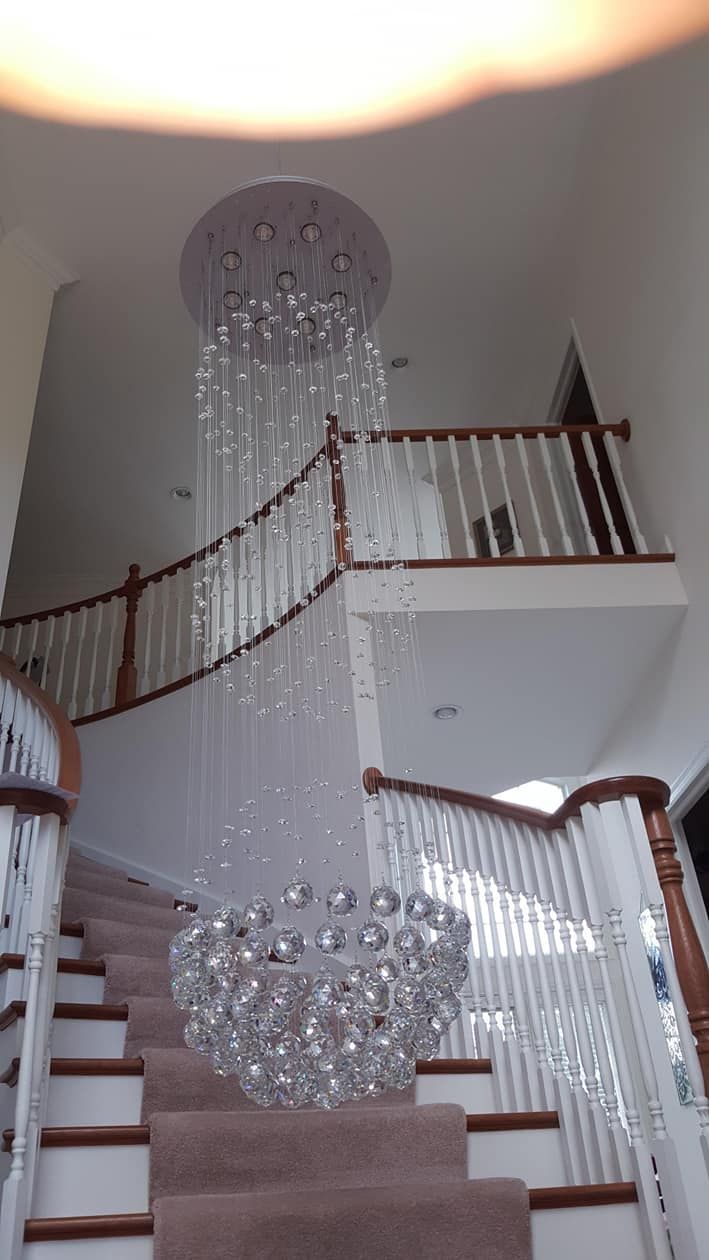 Elegant staircase with curved wooden railing and hanging crystal chandeliers in a bright foyer