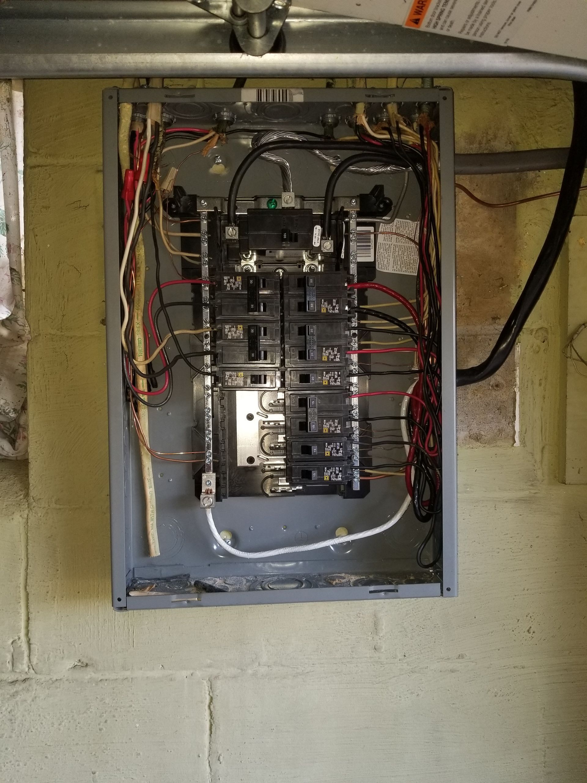 Open electrical circuit breaker panel with exposed wiring in a utility wall recess