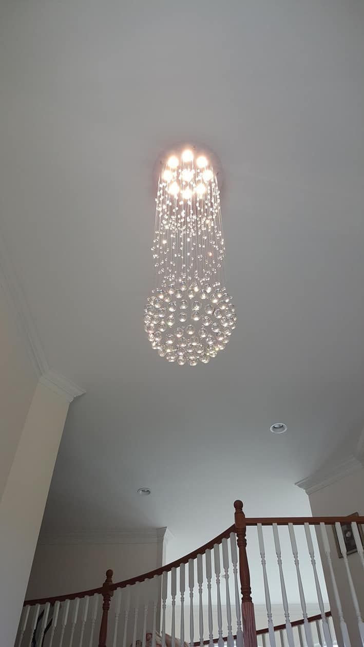 Ceiling view of a glowing modern chandelier above a staircase with wooden railing