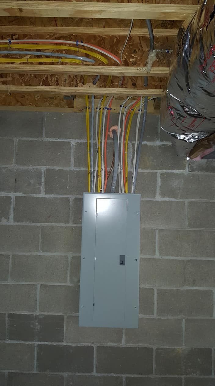 Electrical panel mounted on a cinder block wall under exposed ceiling wiring