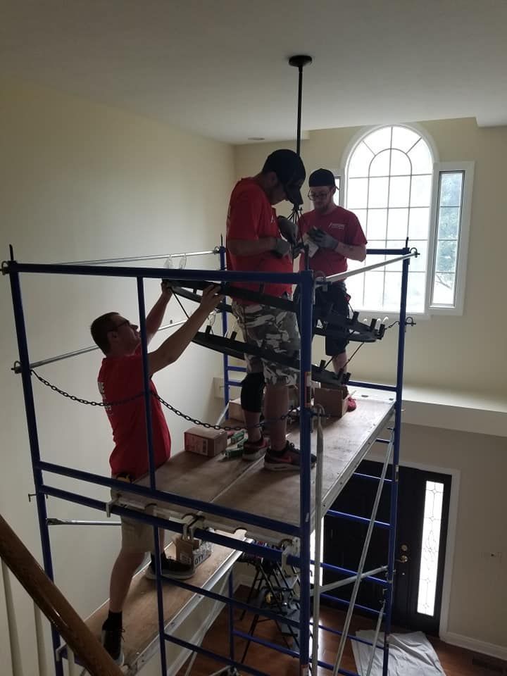 People on blue scaffolding inside a stairwell, working near a tall arched window.