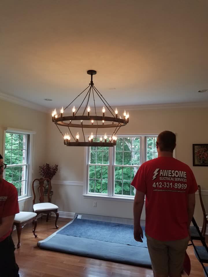 Living room with chandelier, large rug, chairs, and two people in red shirts near windows