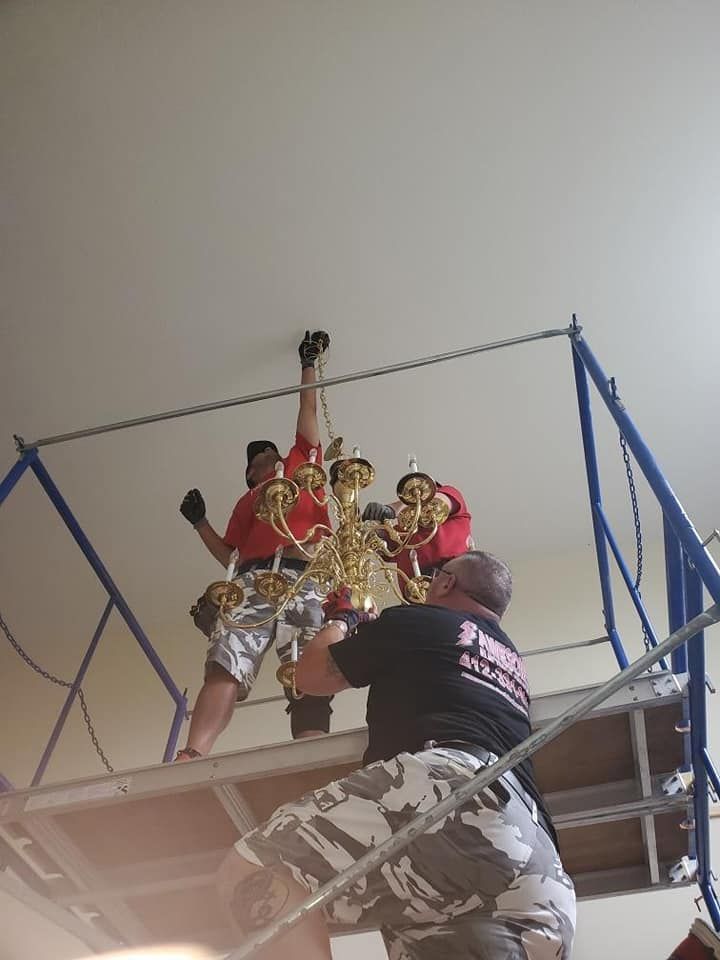 People in red costumes posing on a high platform, with a person in camo below holding up a prop.