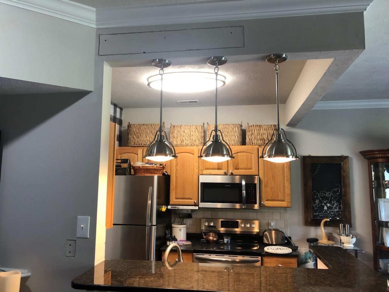 Kitchen with stainless steel appliances, wood cabinets, and three pendant lights over a granite island.