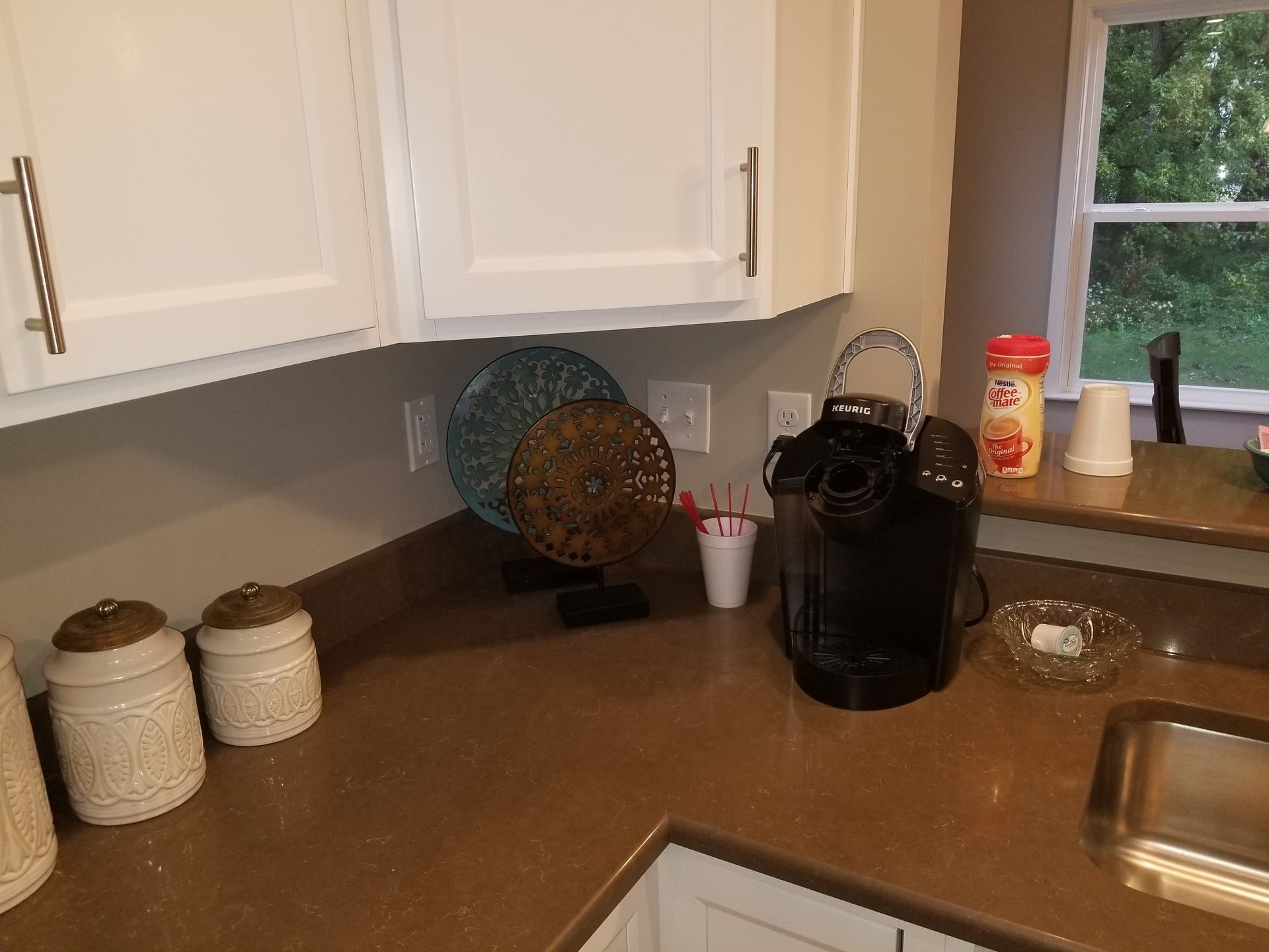 Kitchen counter with white cabinets, coffee maker, paper towel roll, and window above the sink.