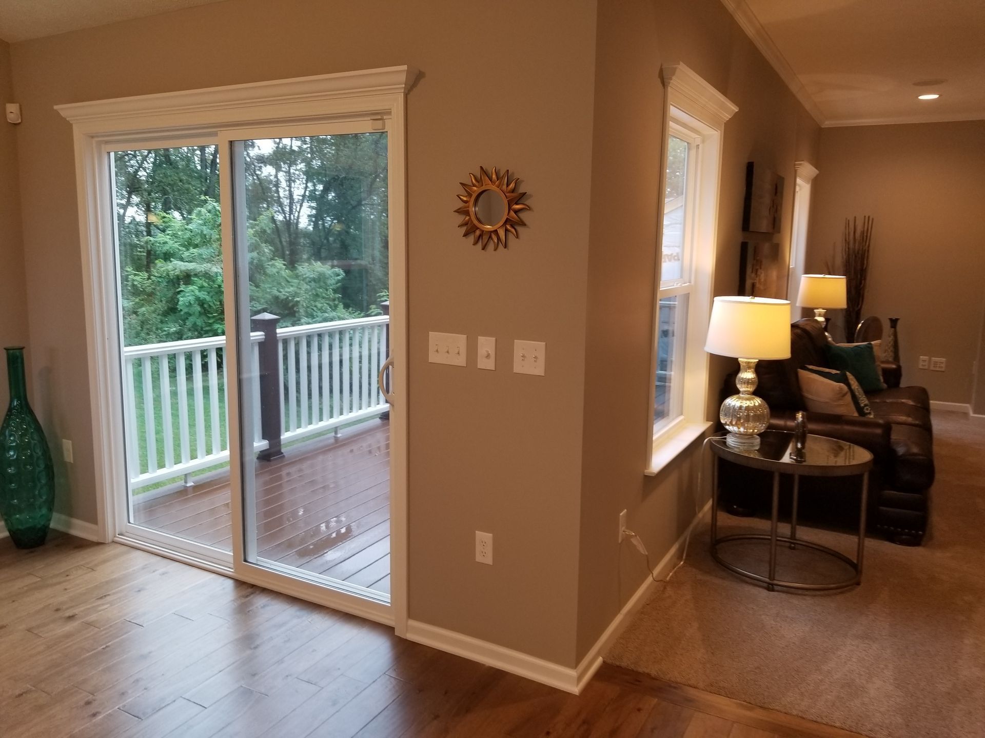 Open living room with sliding glass door to a deck and wooded view, lamp-lit sitting area, and hardwood floors