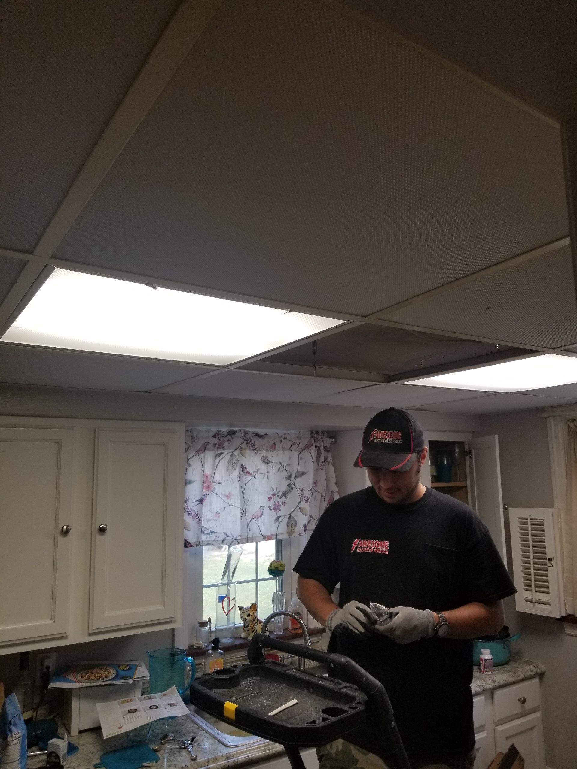 Person in a kitchen works on an open appliance under bright ceiling lights.