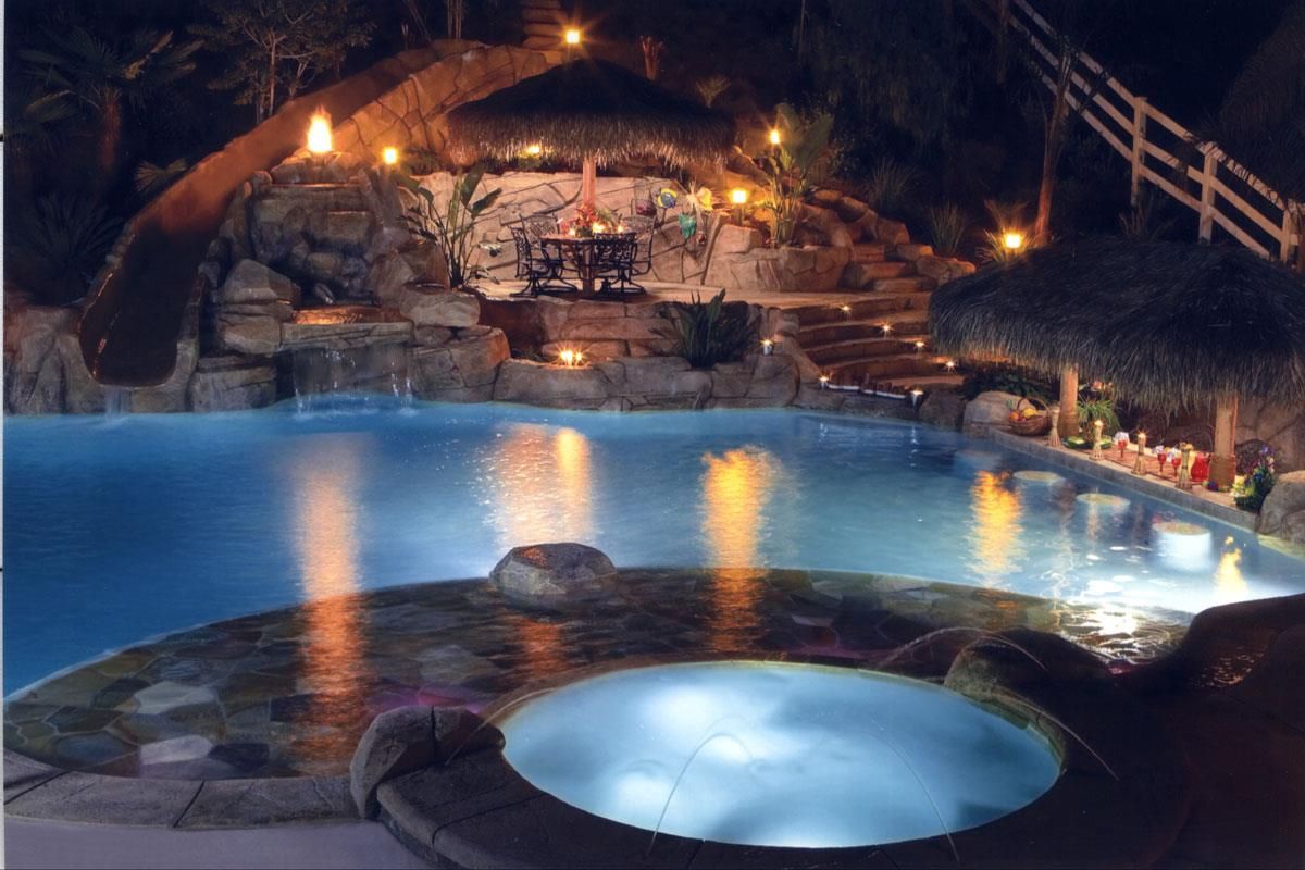 A large swimming pool at night with a hot tub in the middle