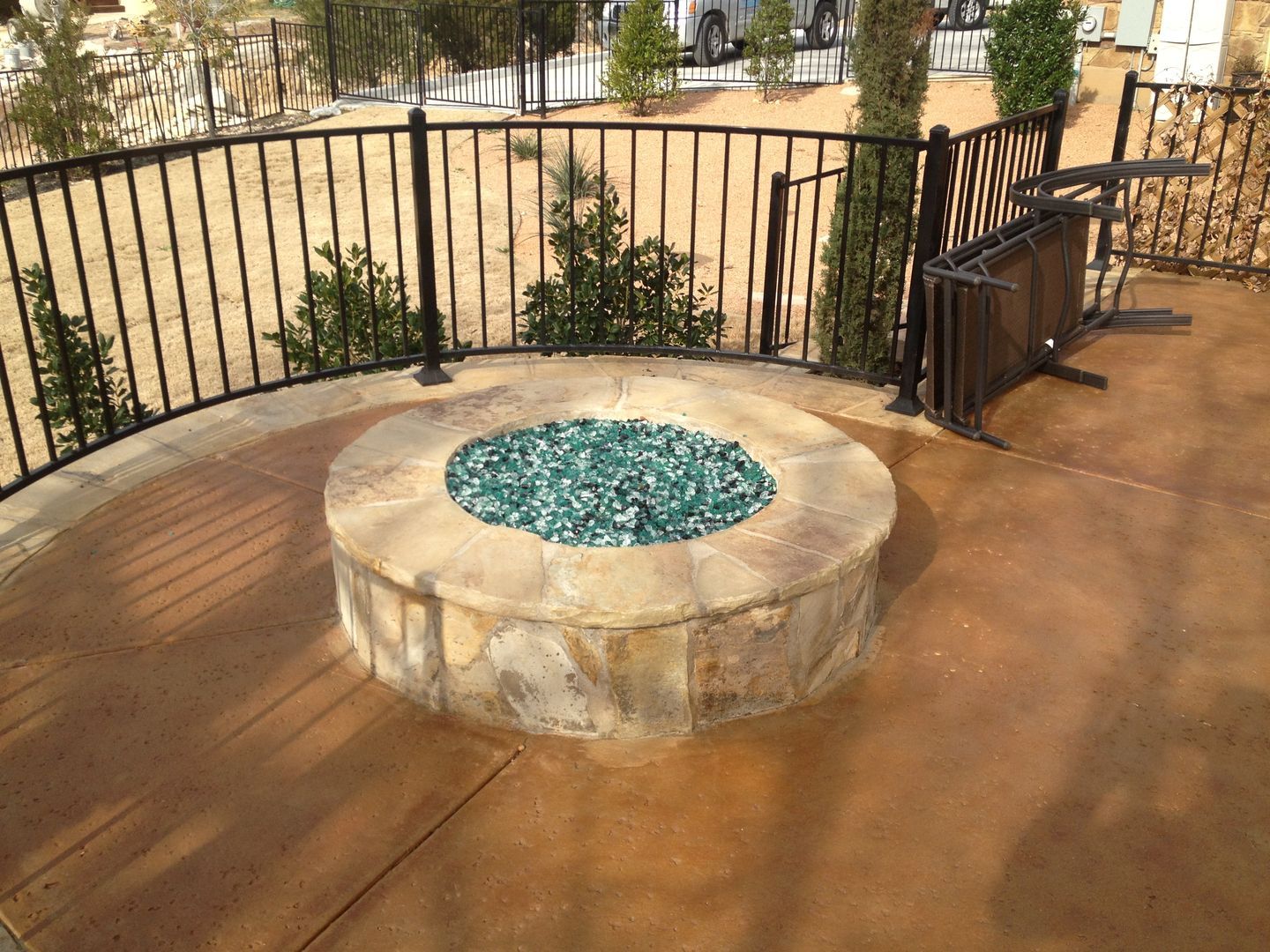 A fire pit is surrounded by a wrought iron fence on a patio.