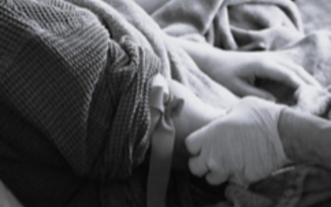 Medical professional's gloved hands applying a tourniquet on a person's arm, preparing for an IV.