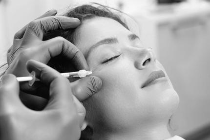Person receiving facial injection near eye. Doctor's gloved hand holds syringe, patient's eyes closed.