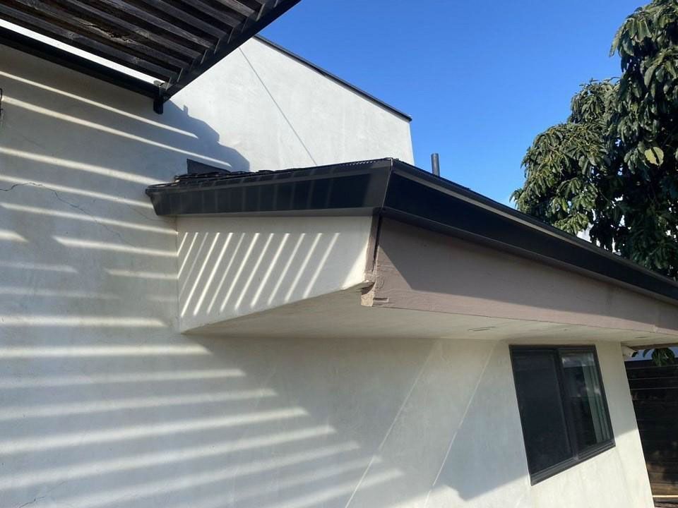 White house eaves with black roof trim casting striped shadows on the wall under a blue sky