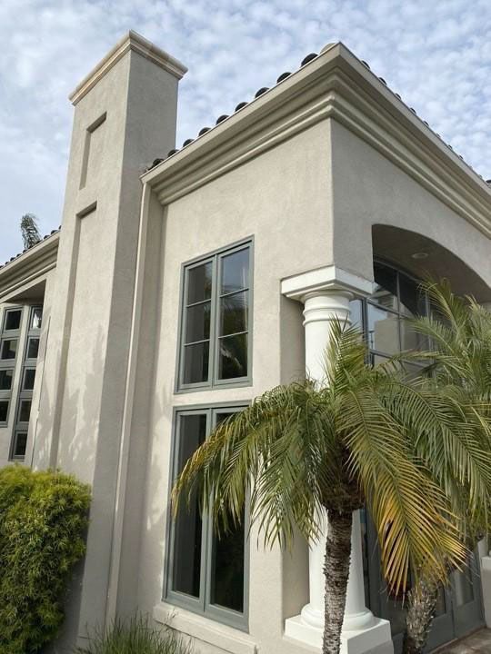 Modern beige stucco house exterior with tall windows, columns, and palm landscaping