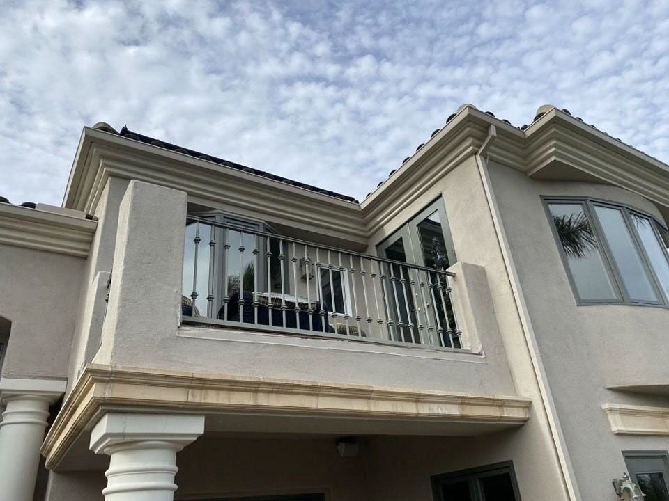 Exterior of a beige two-story house with a balcony and striped awning under a cloudy sky