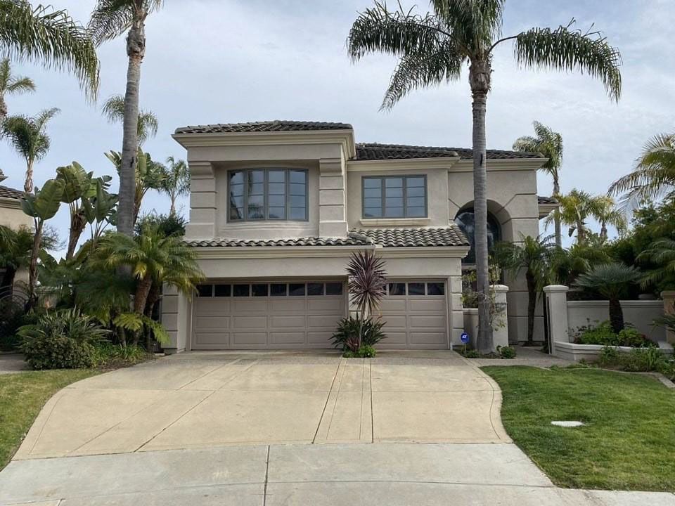Two-story beige house with a double garage, driveway, palm trees, and a manicured front lawn