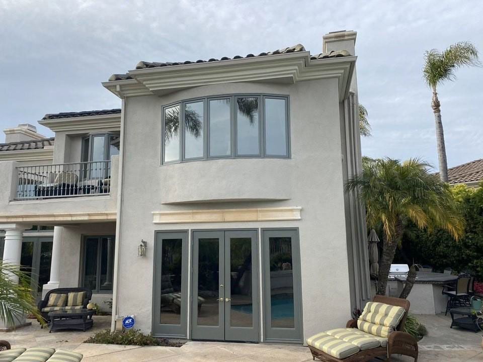 Two-story beige stucco house with glass doors, balcony, and palm trees in the yard