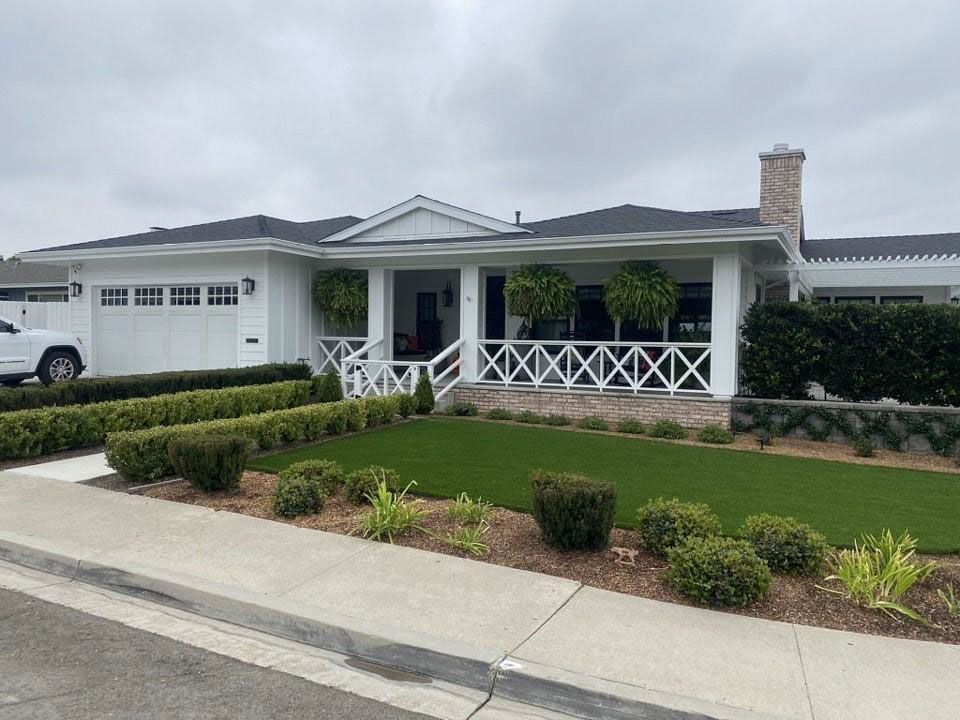 Suburban house with white porch railing, trimmed hedges, and a landscaped front yard.