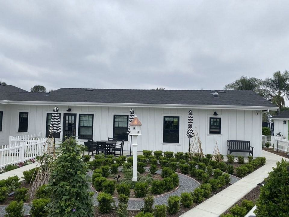 White house with black shutters and a landscaped front garden under a cloudy sky