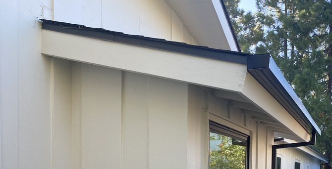 Exterior of a light beige house with a slanted roof and window trim viewed from below
