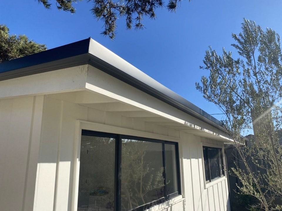 Modern white house exterior with large windows and a blue roof under a clear sky