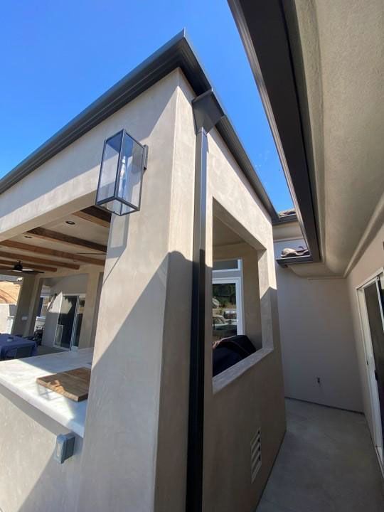 Modern house exterior with beige walls, black roof trim, and a narrow side walkway under a blue sky
