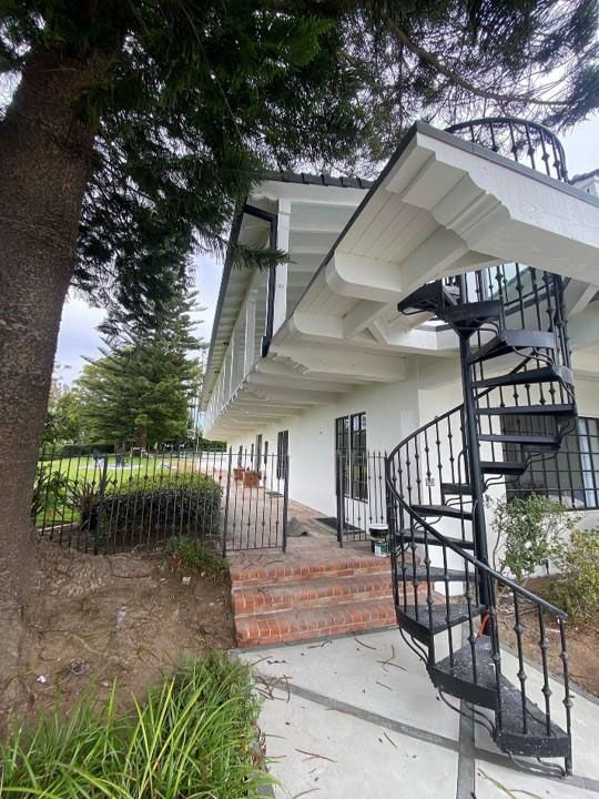 White house exterior with brick steps and a black spiral staircase beside a tree-lined walkway