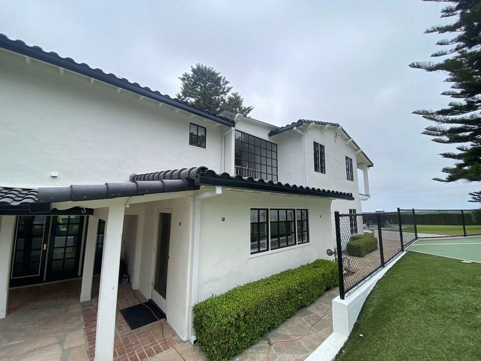 White two-story house with black trim, a tiled walkway, and hedges under a cloudy sky