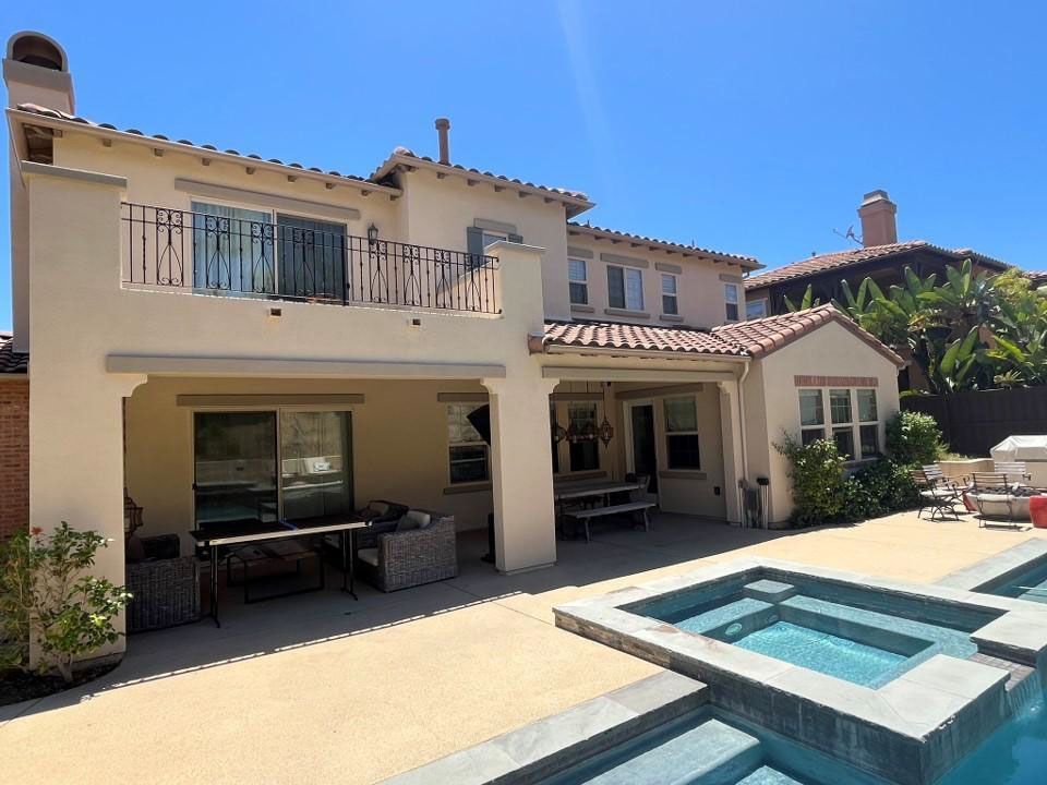 Backyard patio with a two-story beige house, pool, and outdoor seating under a bright blue sky