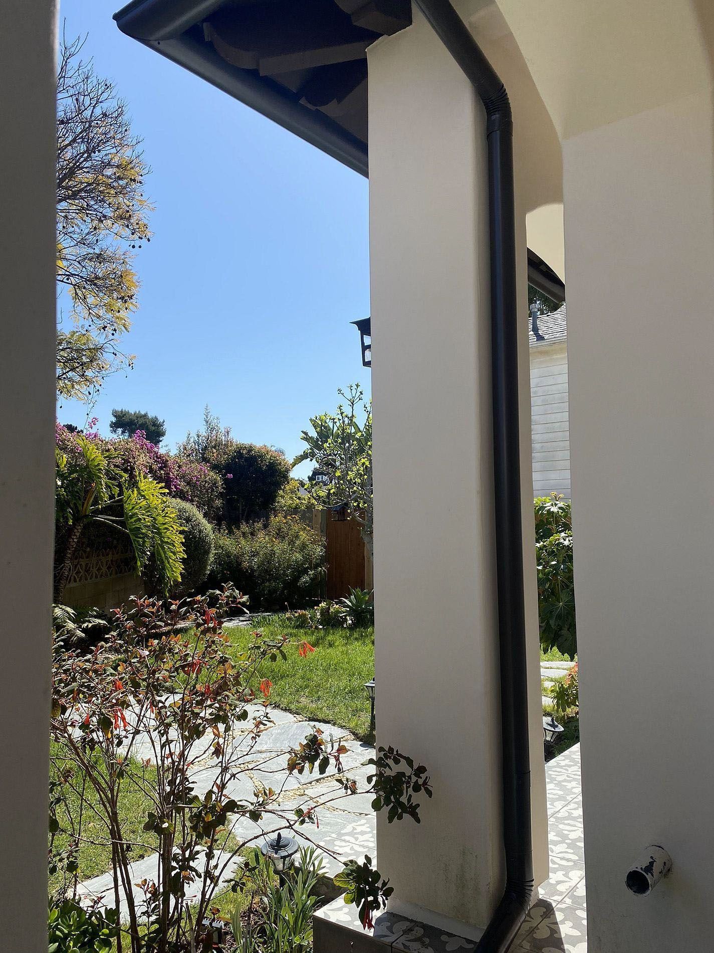 Patio view of a sunny garden with shrubs, lawn, and a house column in the foreground