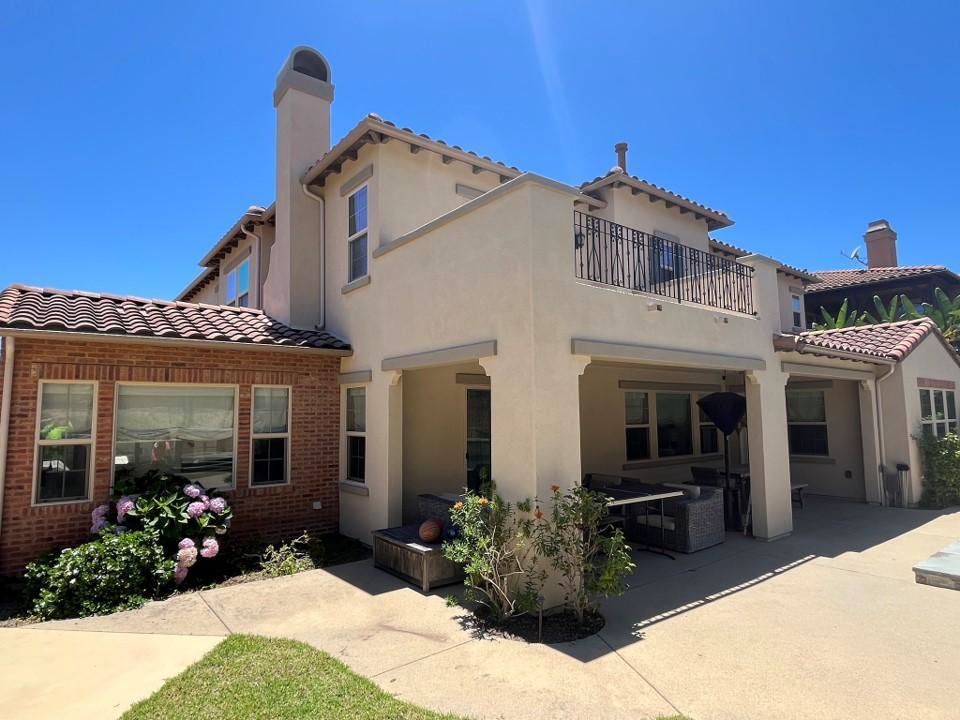 Courtyard view of a beige stucco house with red tile roofs, windows, and potted flowers