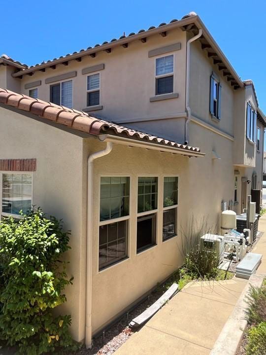 Beige stucco townhouse exterior with tiled roofs, windows, and a narrow side walkway in sunlight