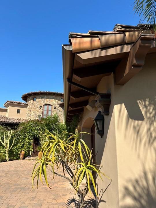 Sunny courtyard with beige stucco walls, stone paving, and potted plants under a blue sky