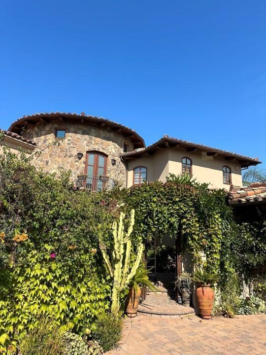 Stone villa covered in ivy with arched entrance and terracotta pots under a bright blue sky