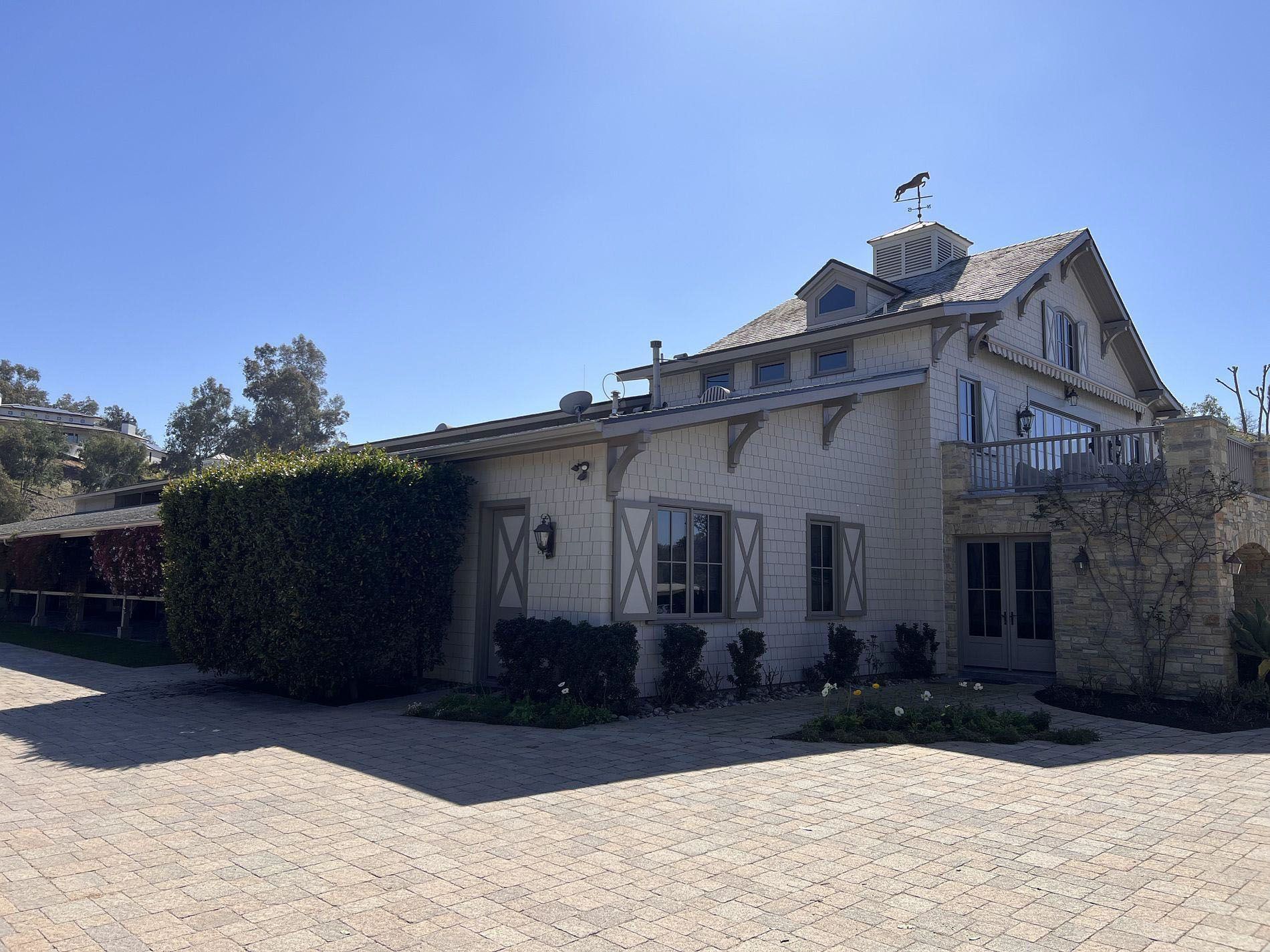 Stone farmhouse with ivy-covered wall and gravel driveway under a clear blue sky