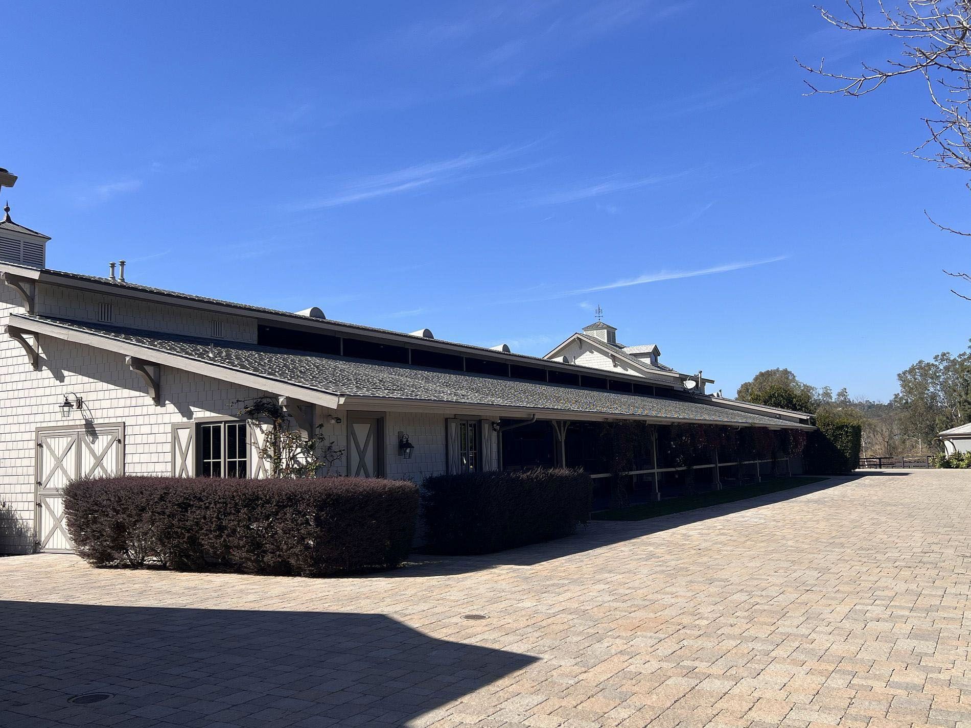 Long white building with a dark roof beside a cobblestone courtyard under a clear blue sky