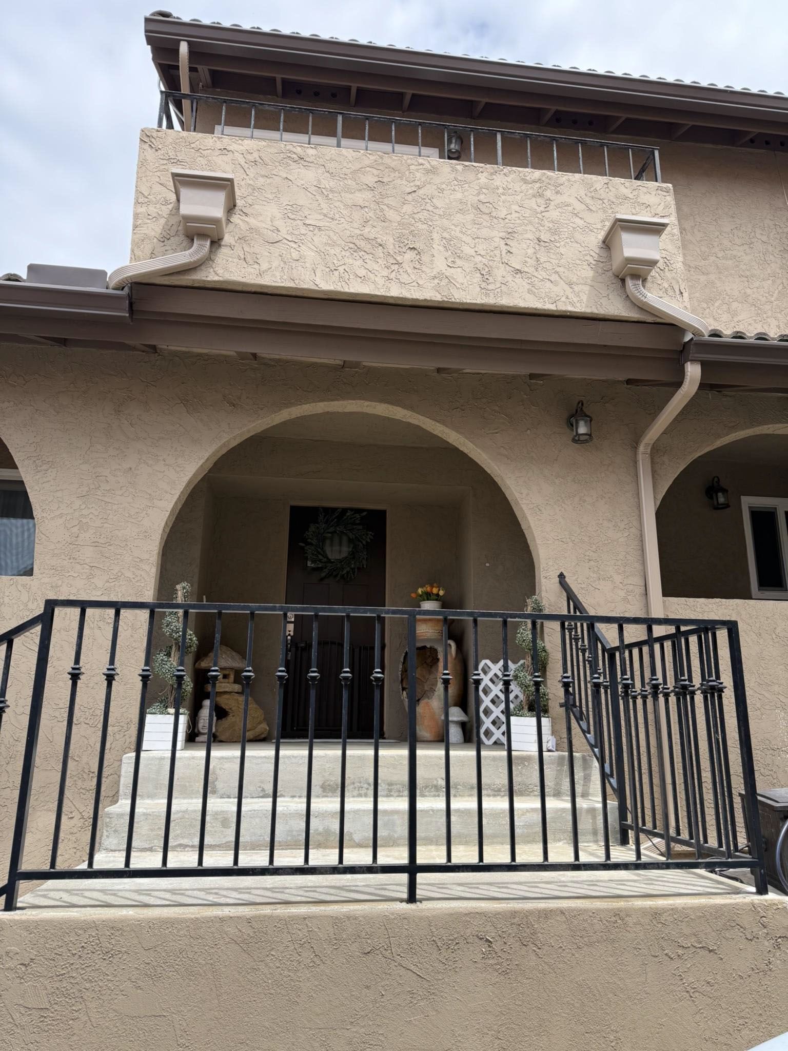 Front view of a stucco house with an arched porch and black metal fence