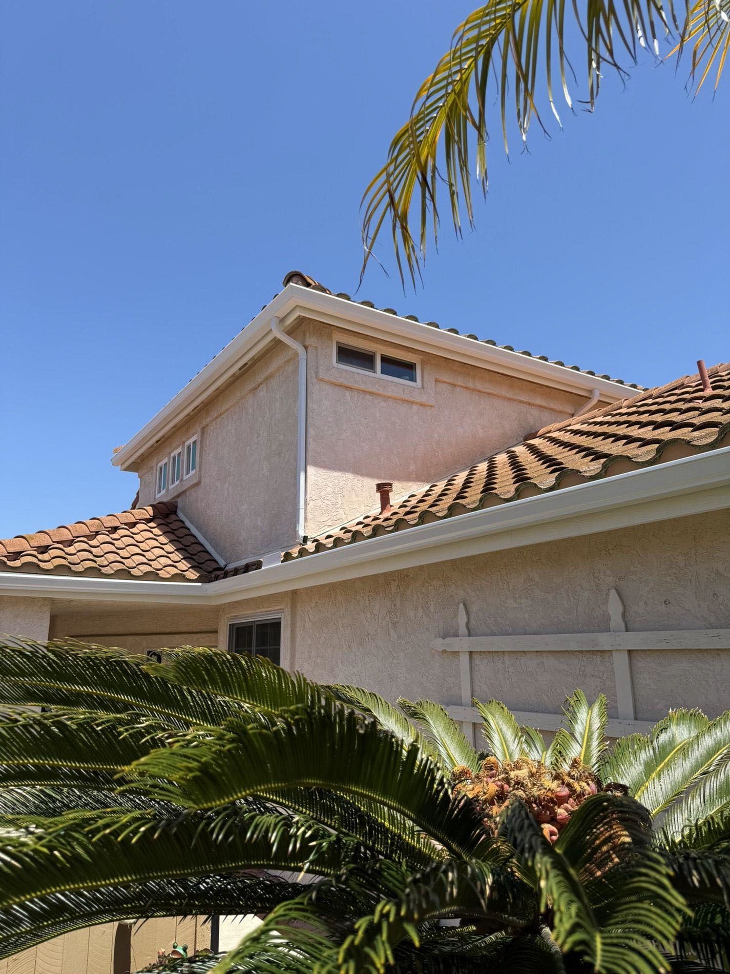 Suburban house with tan stucco walls, red tile roof, and palm fronds against a blue sky